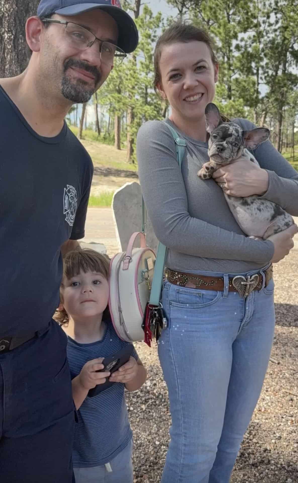 Family with a young son on pickup day, mom holding their new merle Frenchie puppy
